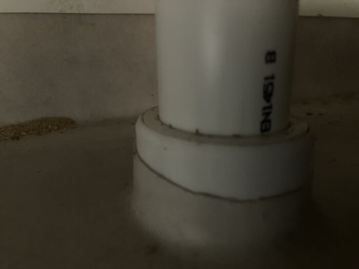 Rör för spillvatten från handfat med uppvikt våtrumsmatta fäst mot plastfläns ("vit donut") nära golv i nyrenoverat badrum.