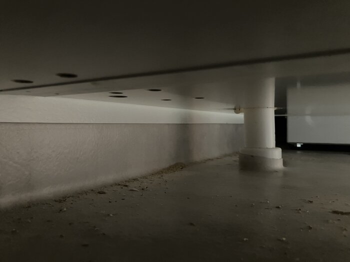 Rörgenomföring för handfatets spillvatten i badrum, våtrumsmatta uppvikt mot vit skyddsrondell runt röret, cirka 6 cm från väggen.