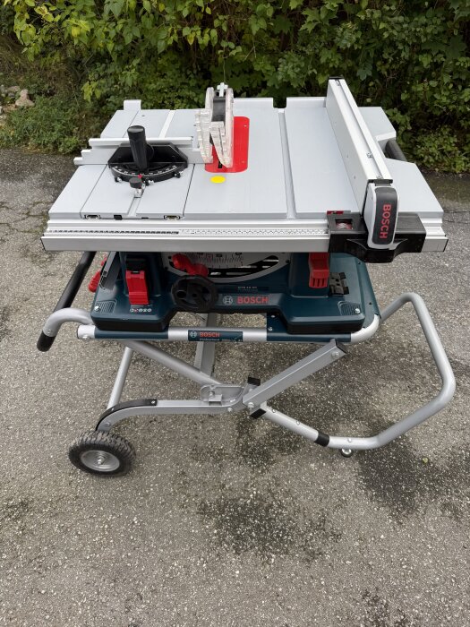 Bordssåg av märket Bosch på ett stativ, placerad utomhus framför grönskande buskar.