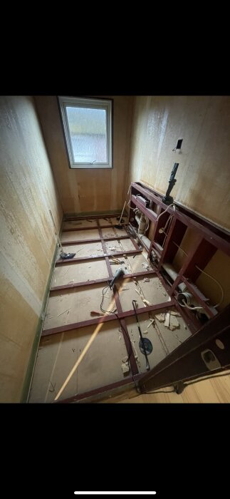 Renoveringsprojekt med synliga metallreglar i golv och väggar, verktyg som vinkelslip och tigersåg på golvet, samt ett fönster i bakgrunden.