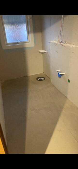 Renoverat badrum med golvvärme och flytspackel, monterade väggar och tak, synliga elkablar och rör, samt ett fönster upptill.