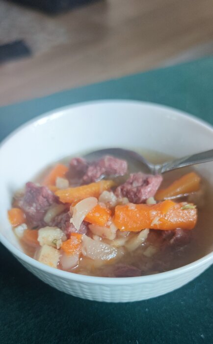 Skål med köttsoppa innehållande fläsk, morötter och buljong, serverad med en sked.