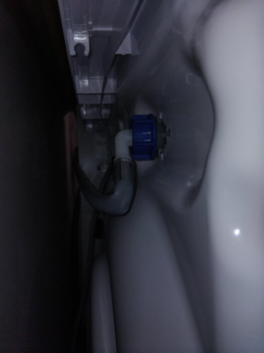 Närbild av en tvättmaskins vattenanslutning som är felvänd och i kläm, med en blå koppling synlig i mitten av bilden.