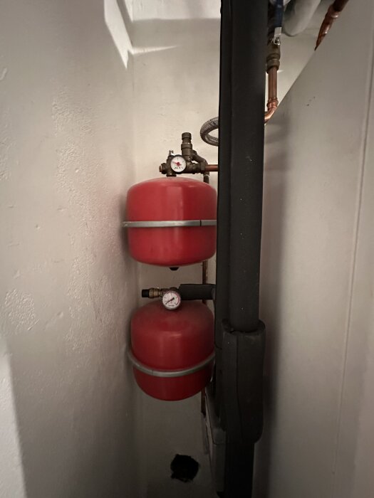 Två röda expansionstankar med tryckmätare, placerade vertikalt i ett trångt utrymme, med kopparrör anslutna.