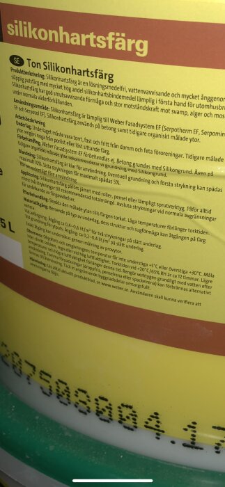 Närbild på en burk med silikonhartsfärg, inklusive bruksanvisning och specifikationer för användning på byggnadsytor.