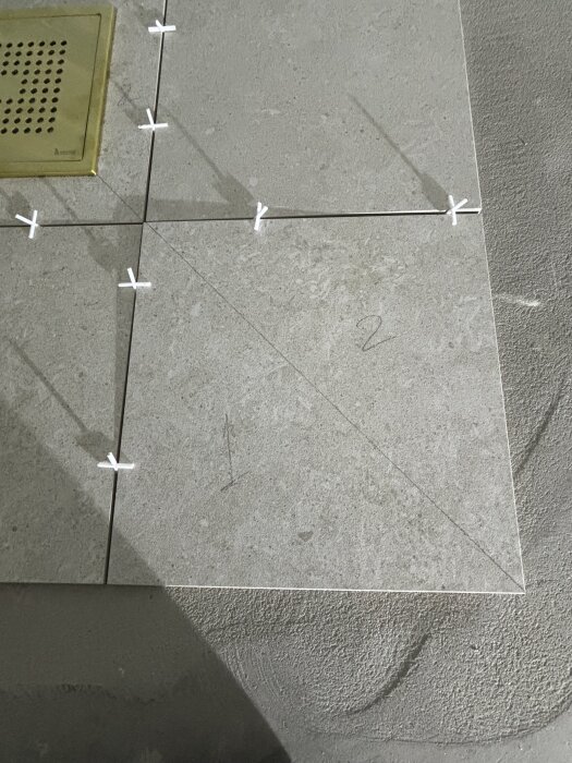 Kakelplattor med kuvertskärning, några numrerade. Plattorna är delvis lagda runt en metallbrunn.