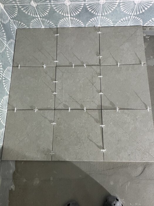 Grå klinkerplattor med kuvertskärning, där distanser syns mellan plattorna. En mönstrad bakgrundstapet i hörnet.