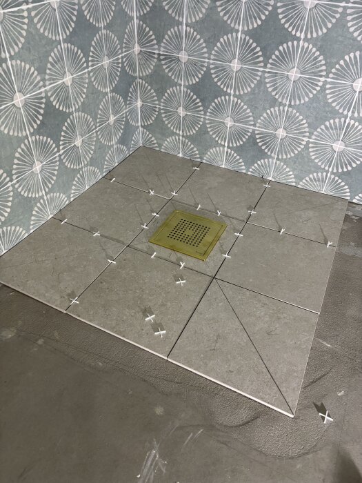 Grå klinkerrutor med vita distanser på golv framför blått kakel med mönster. En gul golvbrunn i mitten av plattorna.