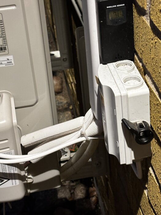 Rören med vit isolering intill gult tegel och en vit enhet med temperatursensor monterad på väggen.