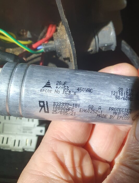 Kondensator märkt "EPCOS 20uF 450VAC No PCB" hålls i handen. Bakgrund med synliga elkablar och komponenter.