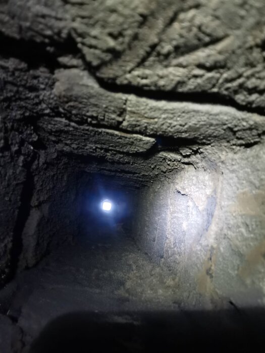 Insidan av en rökkanal med tunn murbruk skikt synligt på tegelväggarna samt ett ljus i slutet av kanalen.