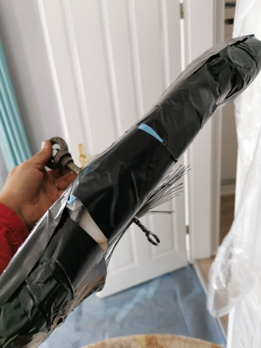 En person håller en modifierad kvadratisk borste, täckt med svart tejp och fastsatt på en stång, för rengöring och justering av skorstenens insida.