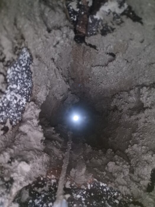 Insidan av en skorsten med nyapplicerat murbruk och ett rep i mitten, sett uppåt mot ljuset från toppen av skorstenen.