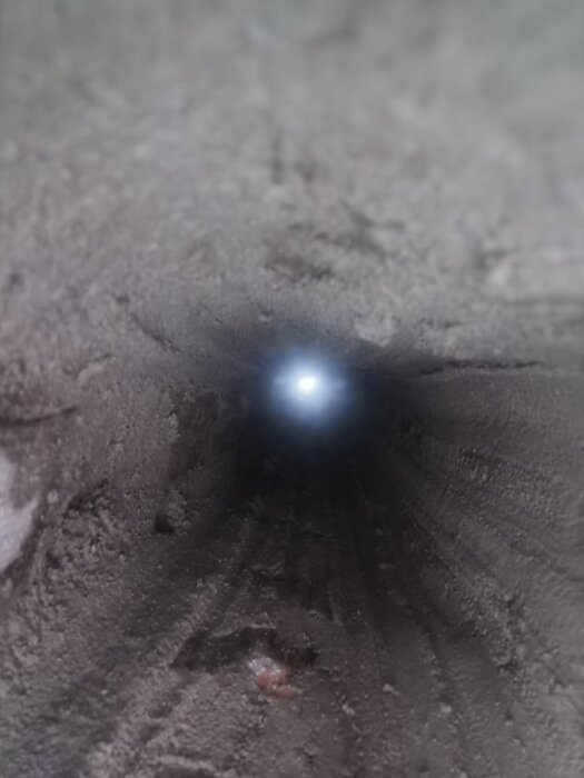 The inside view of a chimney duct, showing rough mortar application and light at the end.