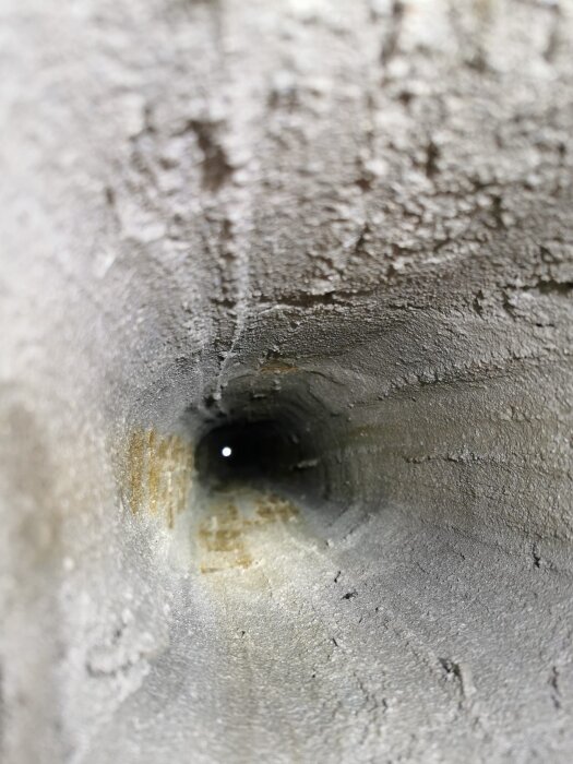 Inside view of a chimney duct showing a textured surface with light visible at the end, illustrating the cleaning and mortar coating process.