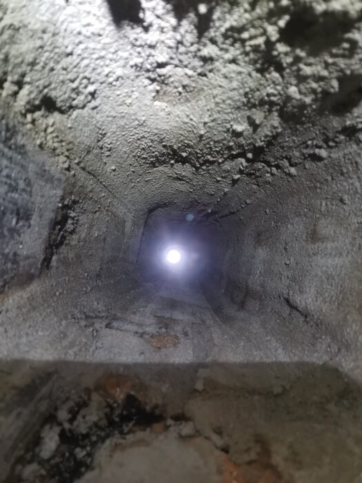 Insidan av en nyrengjord skorsten med synlig mörk öppning i toppen, omgivet av ojämna, murade väggar med rester av bruk.