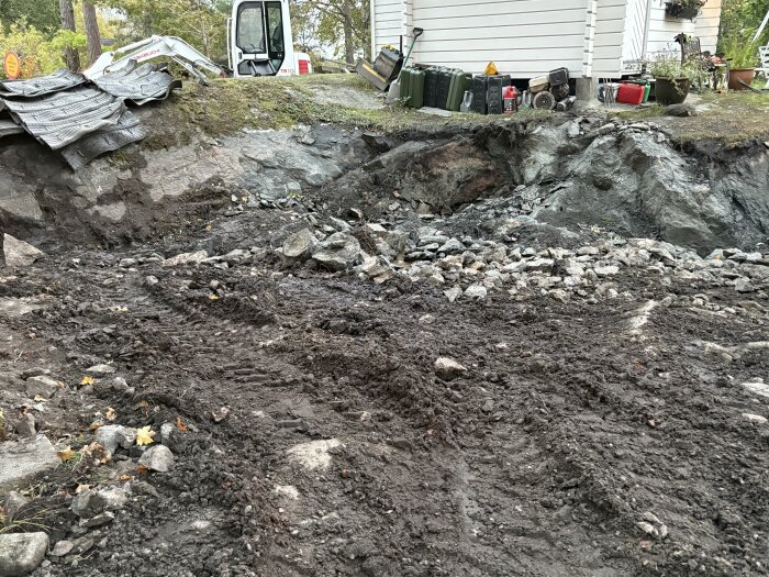 Uppfart med sprängt berg och jord, grushögar spridda över arbetsområdet; skopa av grävmaskin synlig vid kanten.