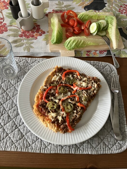 Pizza på bakpulverdeg med köttfärs, ost, tomatsås, lök, vitlök, paprika och jalapeño serverad på en vit tallrik. Salladsgrönsaker på skärbräda i bakgrunden.