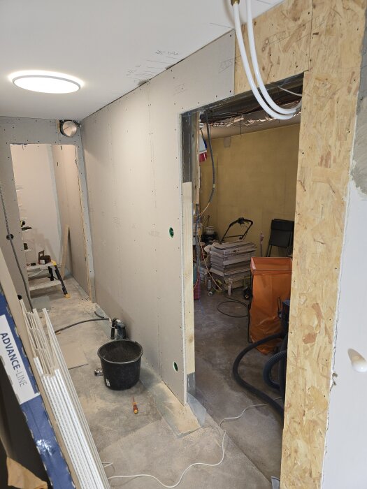 Byggprojekt med reglad vägg under konstruktion; OSB och gipsskivor; verktyg och material synliga; pågående arbete med ventilation.
