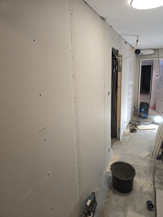 Gipsade väggar i en pågående källarrenovering, byggmaterial och verktyg på golvet, borrad yta för ventilation.