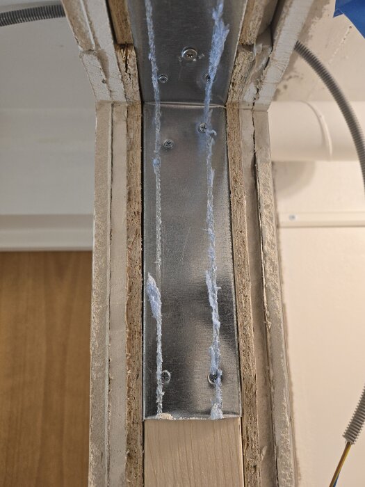 Vy av en del av en byggd vägg med gipsskivor och synlig metallregel, skruvad fast med blå isolering som sticker ut längs kanterna.