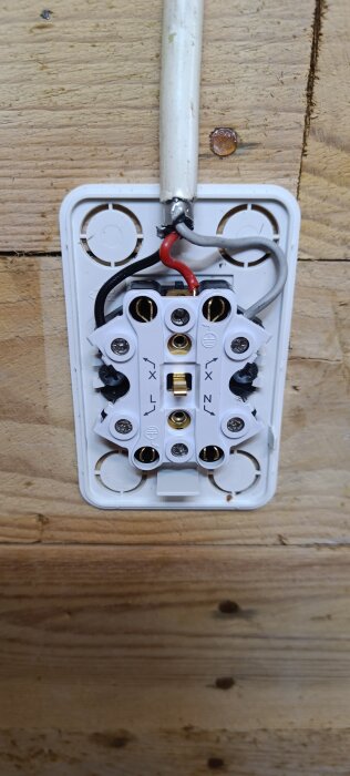 Elkontakt monterad på trävägg med synliga ledningar, där röd kabel används som jordning.
