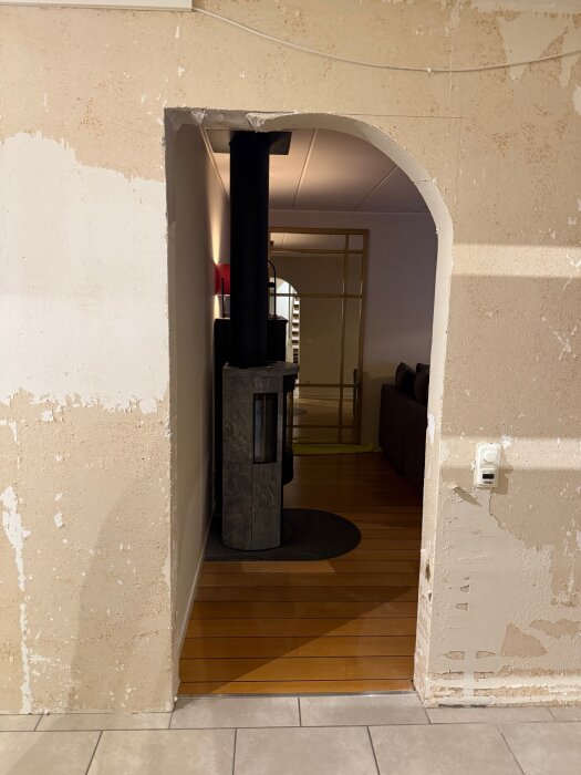 Ett halvrenoverat valv i en hall, med skadade väggkanter. En kamin i rummet bortom valvet och golvet är delvis av trä och kakel.