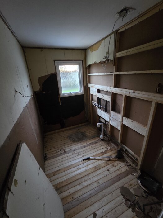 Renovering av golv i ett rum med blottade väggstommar, verktyg på golvet och en golvbrunn, förberett för golvvärme och klinkers.