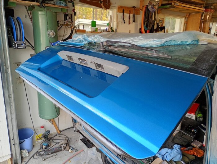 BlÄ baklucka pÄ en Volvo i garage, vÀntar pÄ montering och dekaler. Verktyg och utrustning syns i bakgrunden.