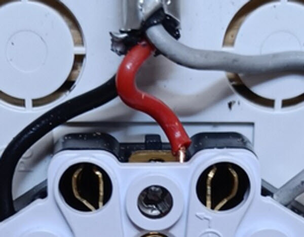 Anslutningspunkt med två hål, en till vänster och en till höger om en skruv, för röda och svarta kablar i en elektrisk installation.