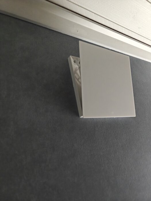 Vit ventilskydd på mörk vägg med öppning som riktar luftflödet åt sidorna.
