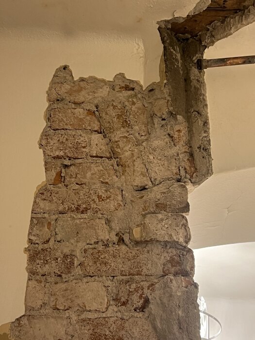 Gammel murvegg med slitt puss og synlige røde murstein, delvis dekket av et tynt lag med hvit maling.