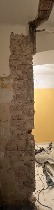 Ruvegg avdekket under renovering, viser eksponerte murstein og verktøy på gulvet. Lys gul vegg i bakgrunnen.
