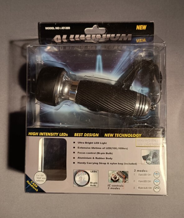 Förpackad ficklampa med text om LED-teknik och fokusfunktion. Svart gummihandtag och flera ljuslägen visas på kartongen.