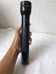 En person håller i en svart Maglite-ficklampa mot en vit bakgrund.