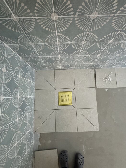 Klinkergolv med snygga, raka snitt och mönstrade väggplattor, gul golvbrunn i centrum.