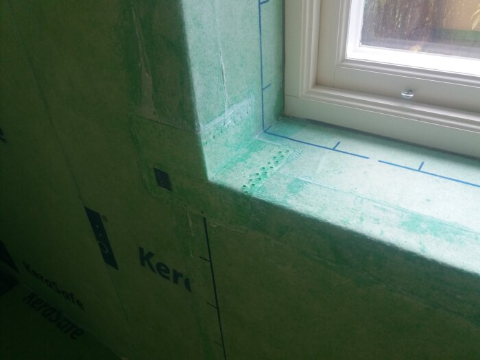 Grön vattentät skiva runt ett fönster i ett badrum under konstruktion, med markerade linjer för kakelinstallation.