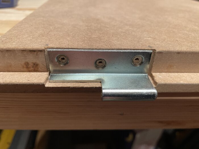 Försänkt metallgångjärn monterat på en träram, med tre skruvar synliga och precisionsfräsning för att säkerställa att dörren hänger rakt.