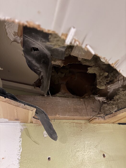 Hål genom vägg med borttagen isolering och en synlig takstol, skuren för ventilationsrör.