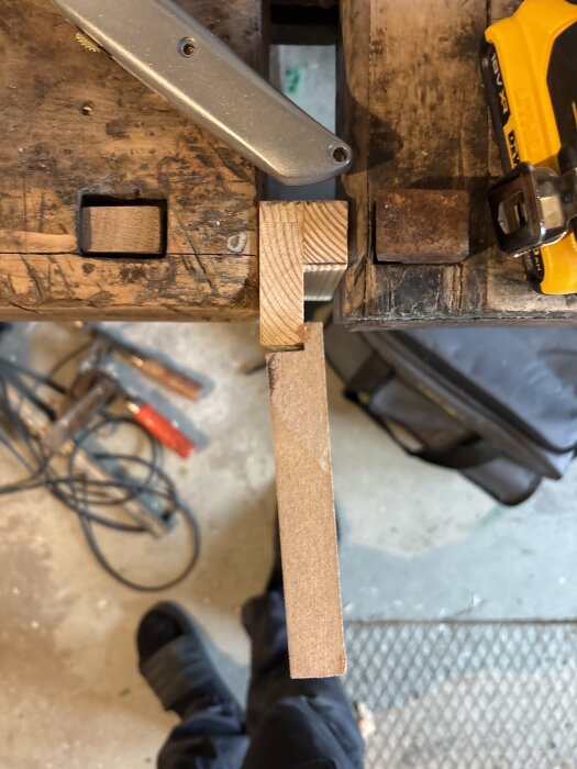 Träarbetsbänk med fastspänd träbit och verktyg i bakgrunden, fokus på gångjärnsmontering.