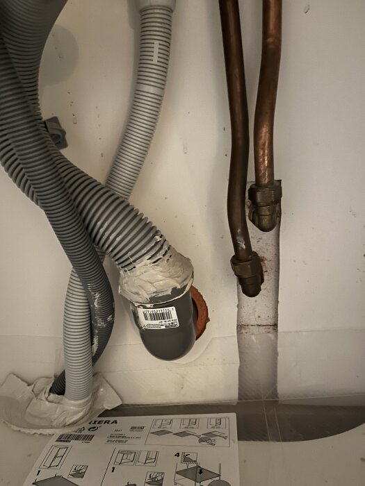 Grå gummislangar och kopparrör i ett utrymme med monteringsinstruktioner i förgrunden.