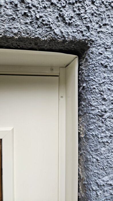Ny källardörr med plåt runt kanterna mot grov puts, fokus på hörnens montering.