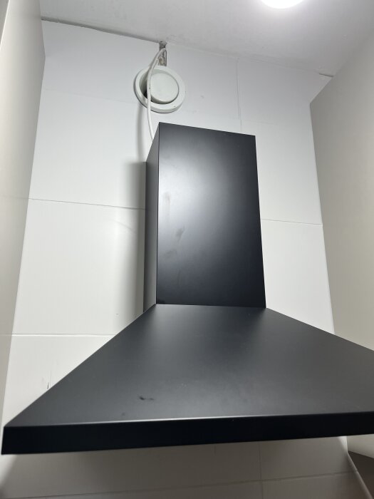 Svart köksfläkt med sladd ansluten till taket, monterad i en bostadsrätt.