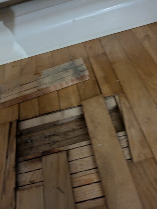 Gammalt golv med synlig fuktskada, stavar under parkett lyfta för renovering i radhus från 60-talet.