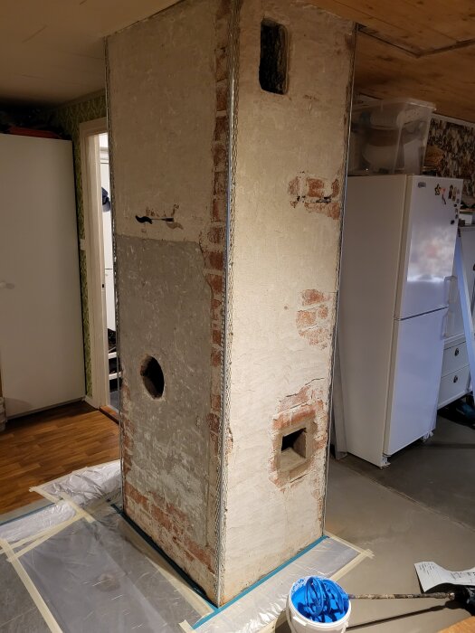 Murad hörn med hörnförstärkningar, redo för primer, i ett rum med trägolv och en synlig kyl i bakgrunden.