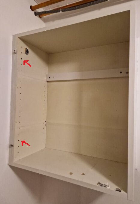 Tom vägghylla med skruvar i hålen för hyllstöden, markerade med röda pilar, tredje hålet uppifrån och nedifrån.