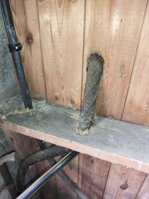 Gammal tjärkabel som går in genom en trävägg i ett uthus.