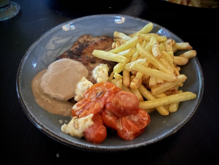Tallrik med kryddad fläskkarré, pommes frites, grönpepparsås och ugnstekta tomater med mozzarella.