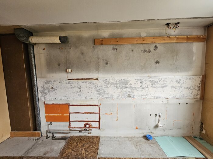 Köksvägg under renovering med synliga rör, betongvägg och träregel upptill, ventilationstrumma till vänster och diverse markeringar och hål i väggen.