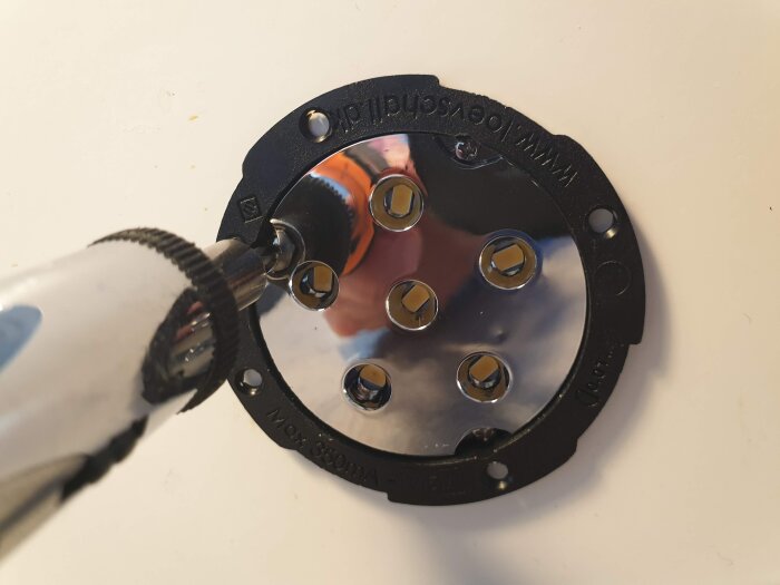 Skruvdragare demonterar LED-möbelspotlight på en metallplatta med flera monteringshål.